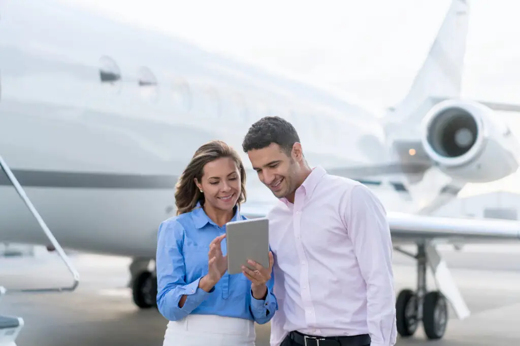 Two people reviewing a tablet beside a private jet.